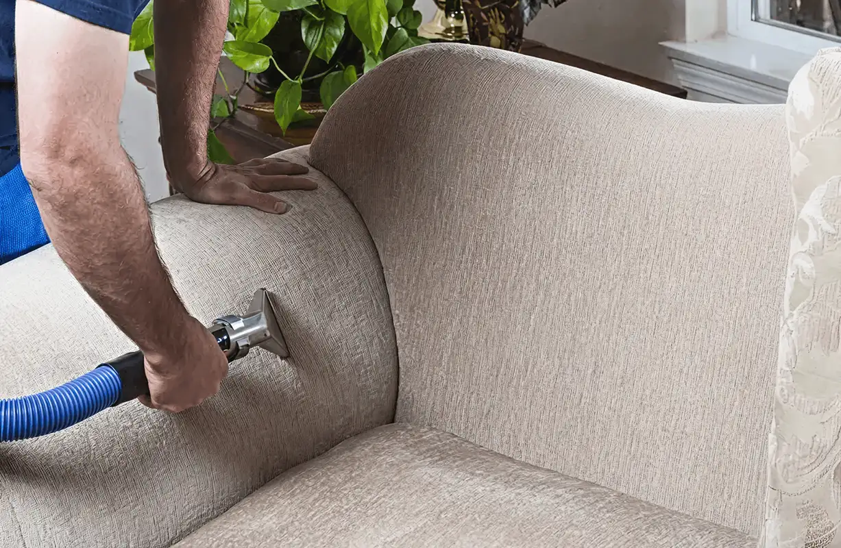 Professional upholstery cleaner deep-cleaning a fabric sofa with a handheld extraction tool and hose, Savannah, GA.